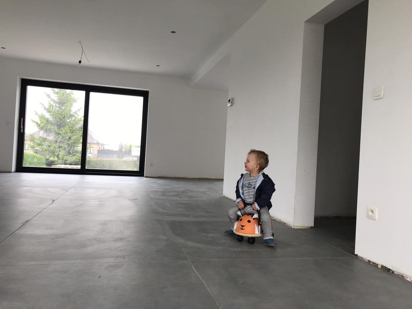 Kind op een loopfiets in een lege nieuwbouwwoning met grote grijze tegels