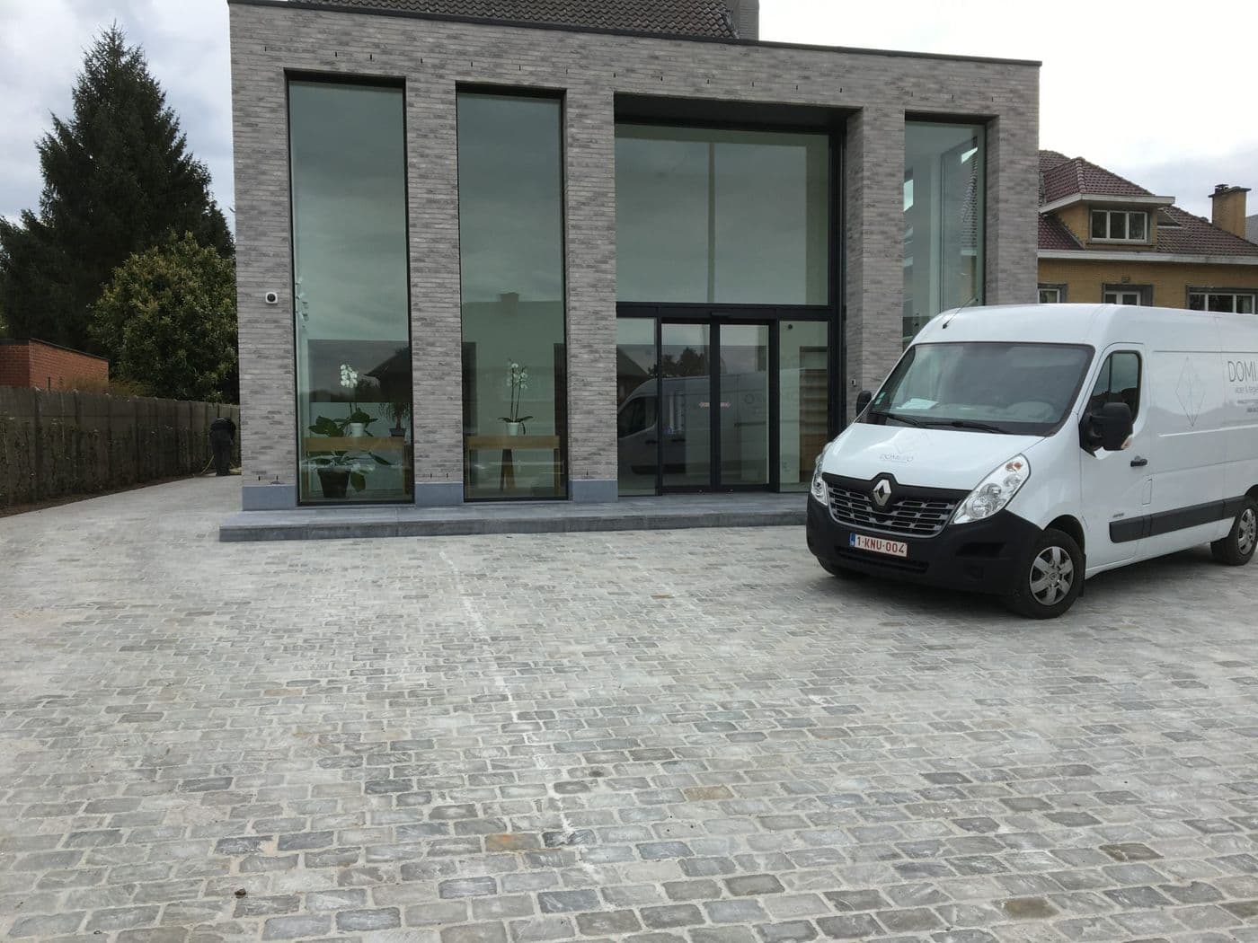 Oprit in kasseien voor een modern gebouw met de bestelwagen van Domino